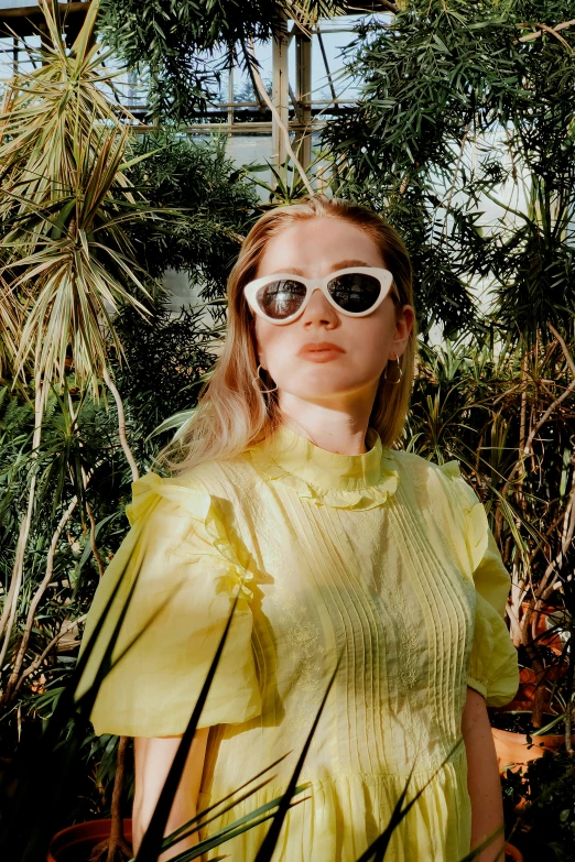 a model wearing sunglasses stands in the middle of plants