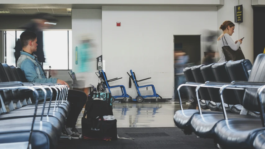 two people standing around an airport next to blue seats