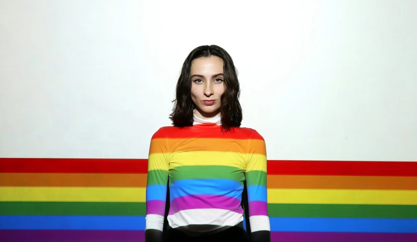 a woman standing in front of a wall with a rainbow painted sweater on