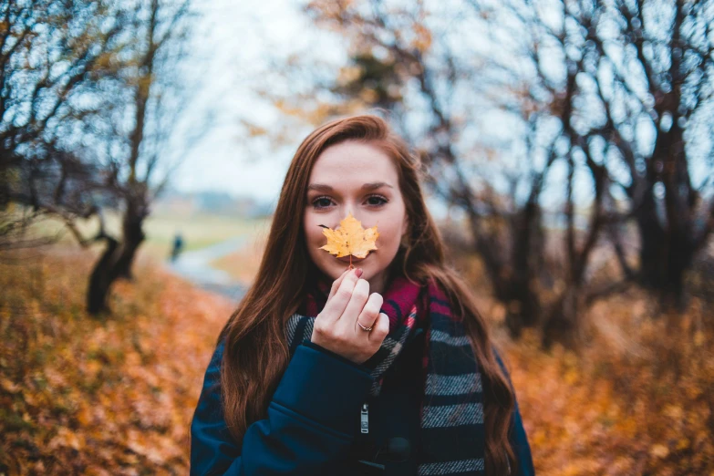 a beautiful woman holding an autumn leaf up to her mouth