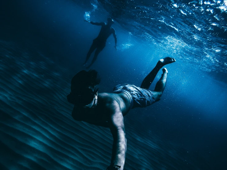 two people dive down from the bottom of a body of water
