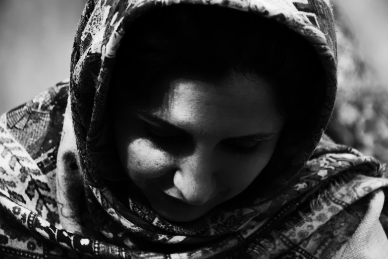 a woman wearing a shawl and a hoodie is looking down