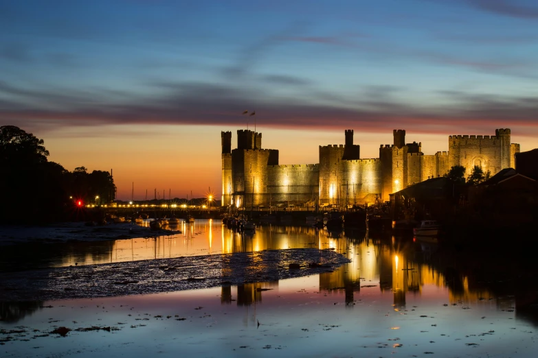 the sunset view of a castle lit up over a body of water