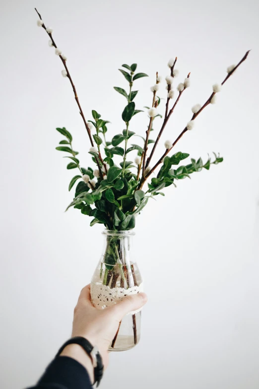 a person holding up a glass vase filled with white flowers