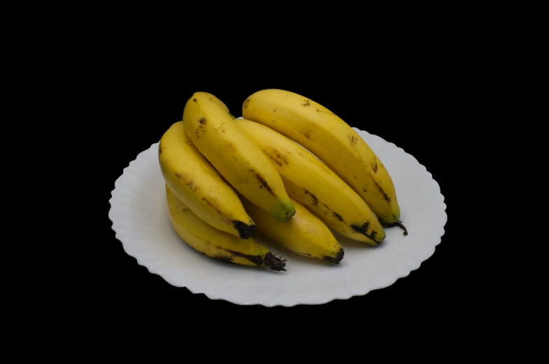 five bananas sitting on a white plate against a black background