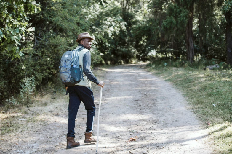 a man walking down a dirt road with a blue backpack