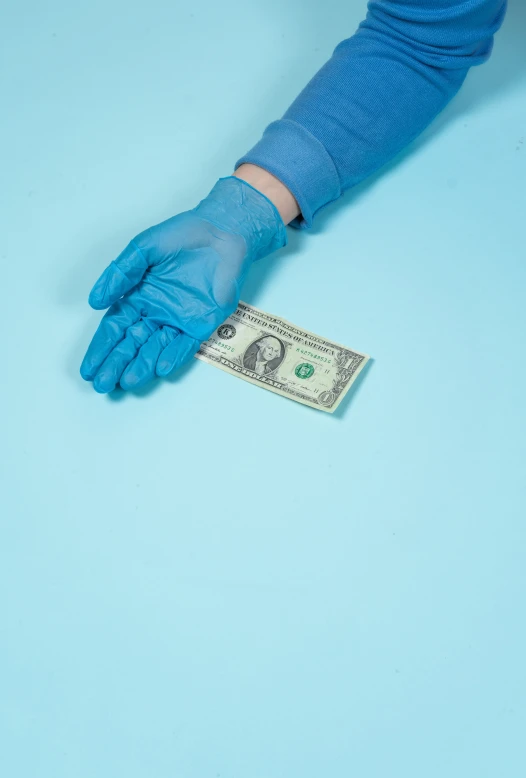 a hand with blue latex gloves holding a twenty dollars bill