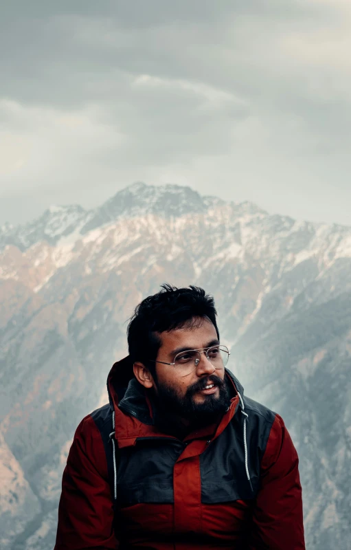 a man with a beard is posing in front of a mountain range