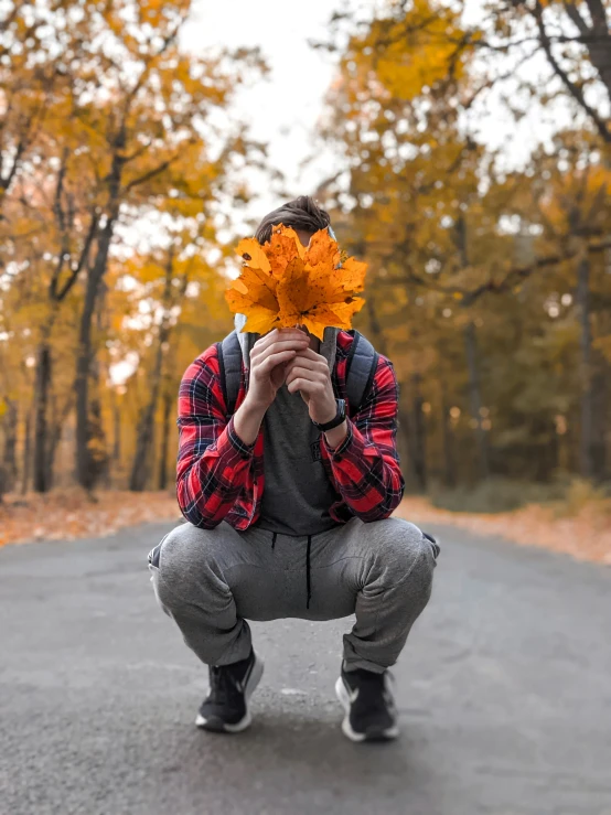 a person kneeling down holding up a leaf in front of their face