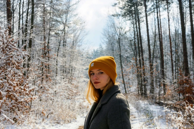 a woman in a hat standing next to a path with trees covered with snow