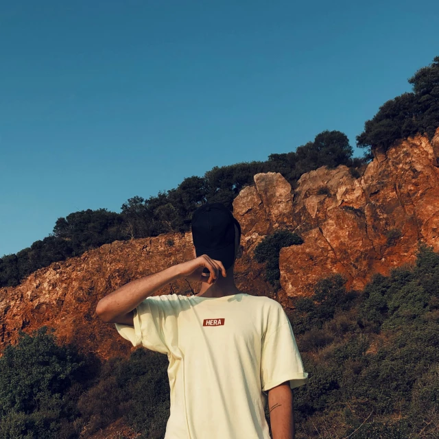 a man in white shirt standing by a rock face