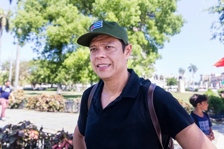 man in blue polo shirt and green hat standing on sidewalk