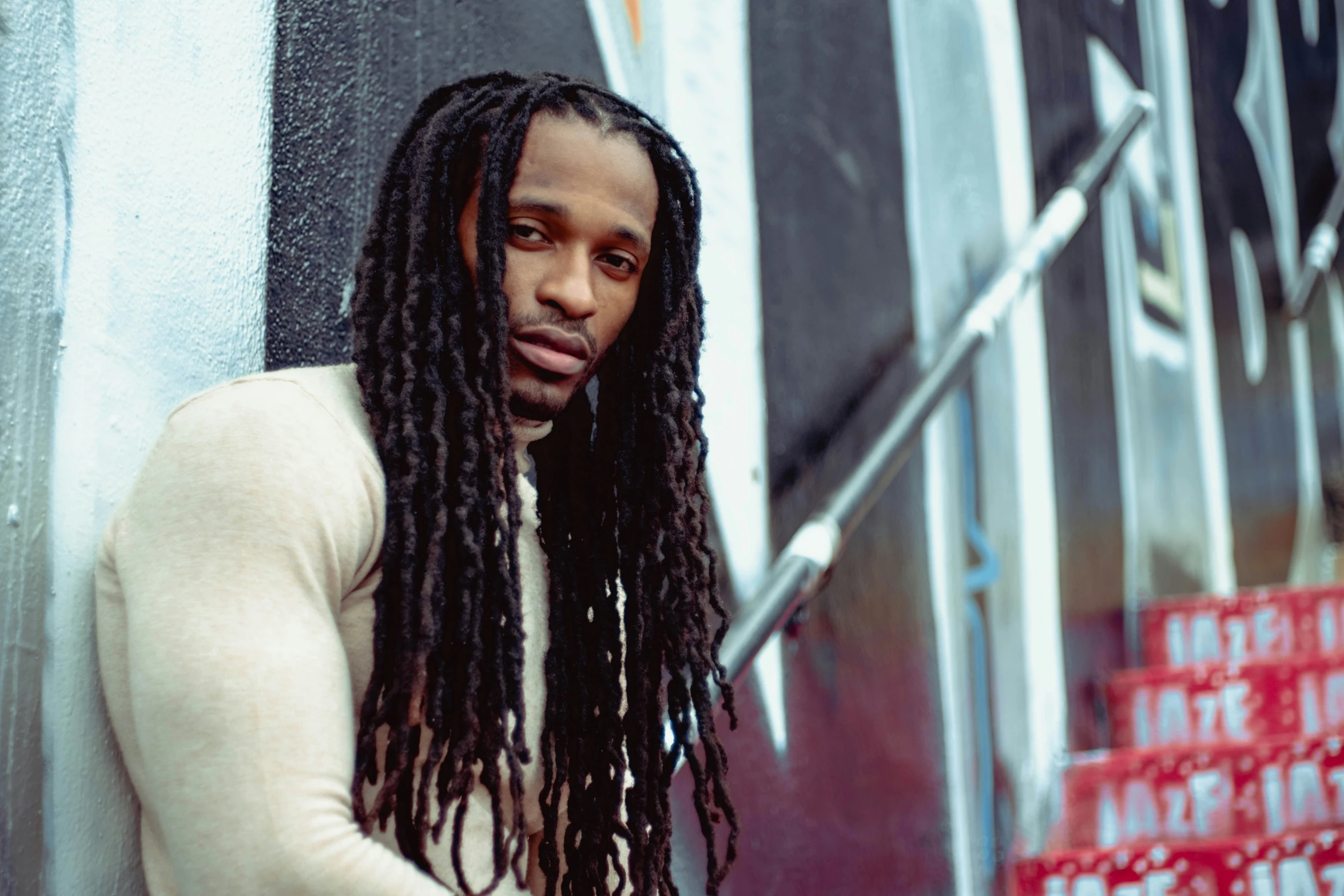 a man with long, dread locks leans against a wall