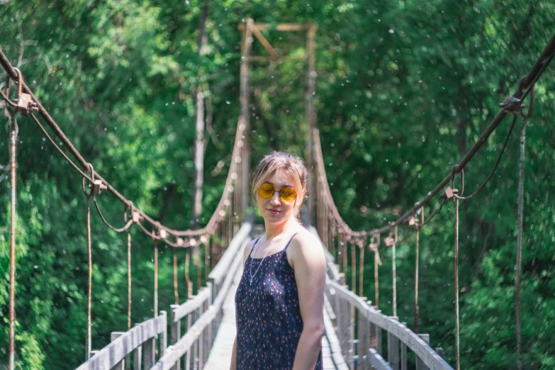 a woman wearing sunglasses poses on a suspension bridge