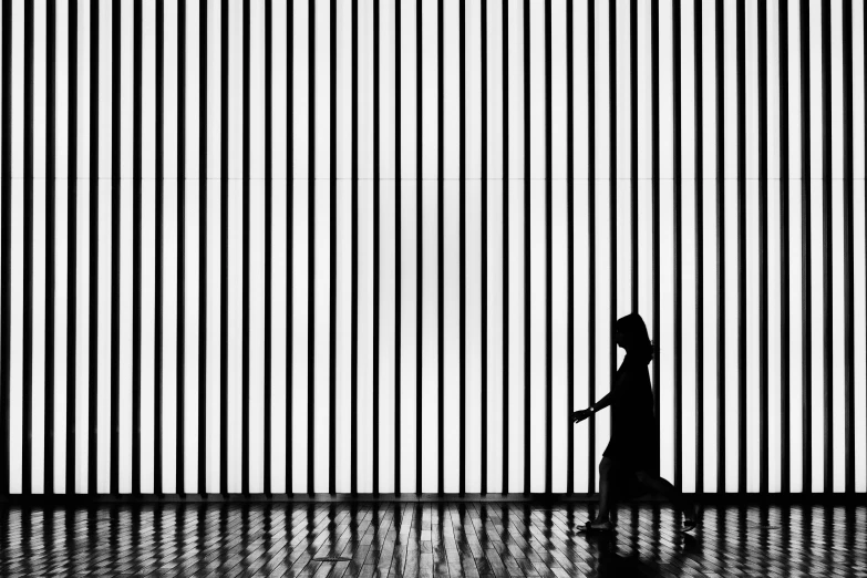 silhouette of a woman walking past a wall made with bars