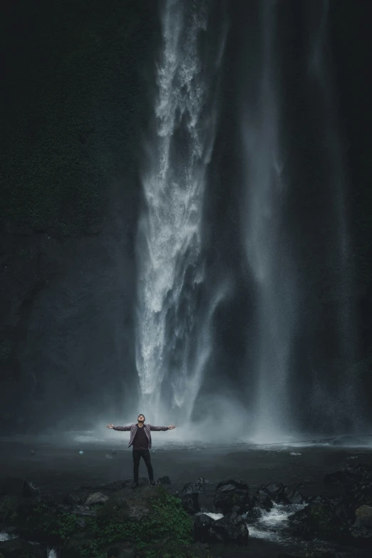 man in front of a tall waterfall with his arms spread