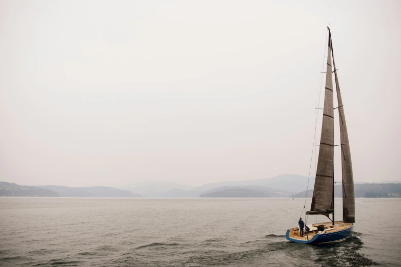 a sailboat traveling along in the ocean on a cloudy day