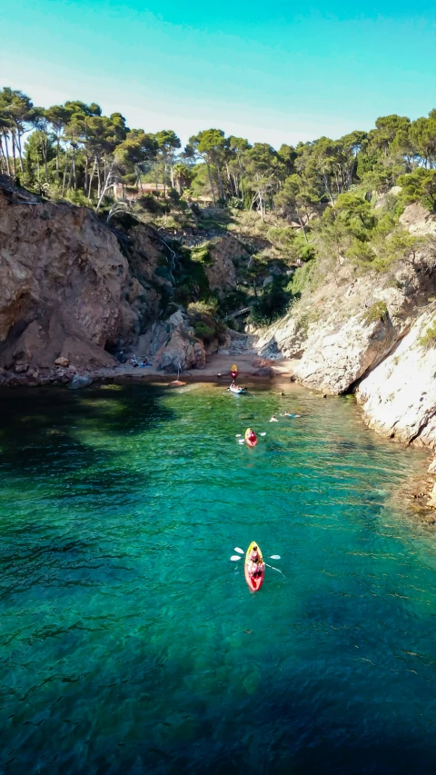 several kayakers in clear blue water beside rocks