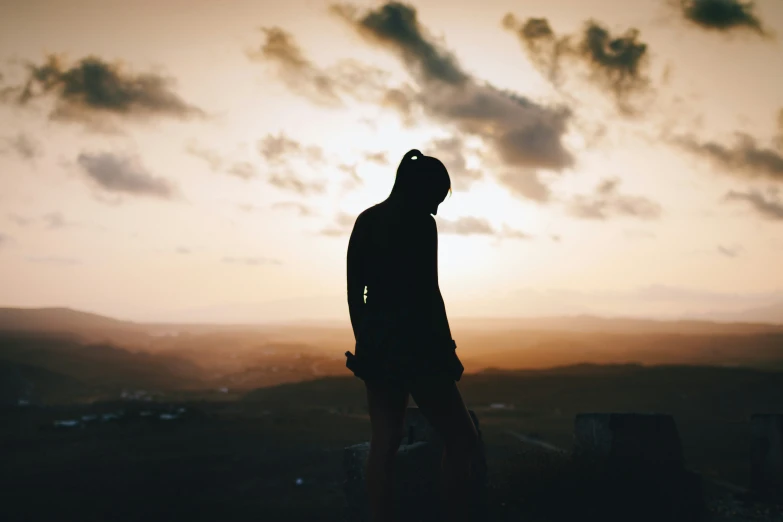 a silhouette of a person standing at the top of a hill