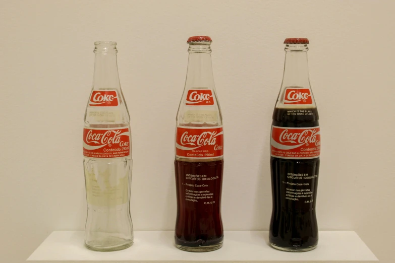 two soda bottles sitting on a shelf one with coca cola