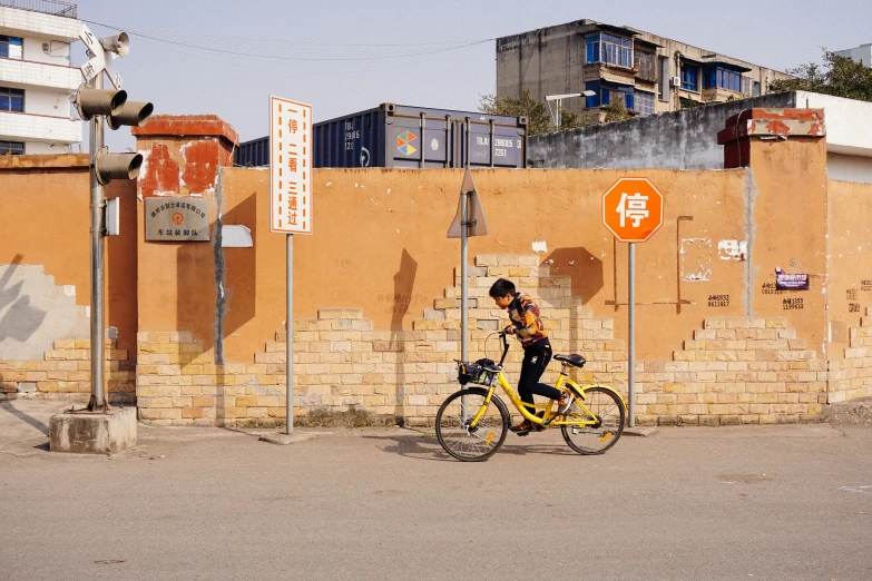 man riding a yellow bike next to a brick wall