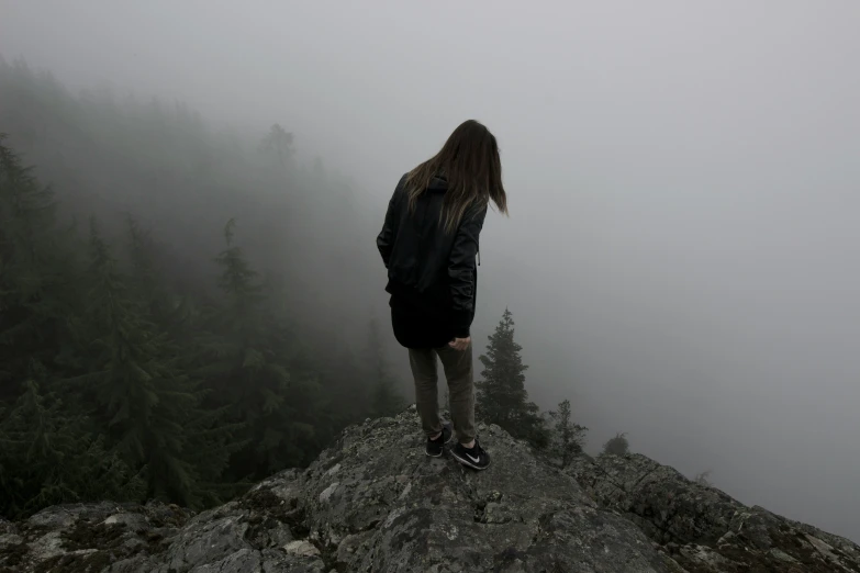 a woman stands on a rock in the middle of fog