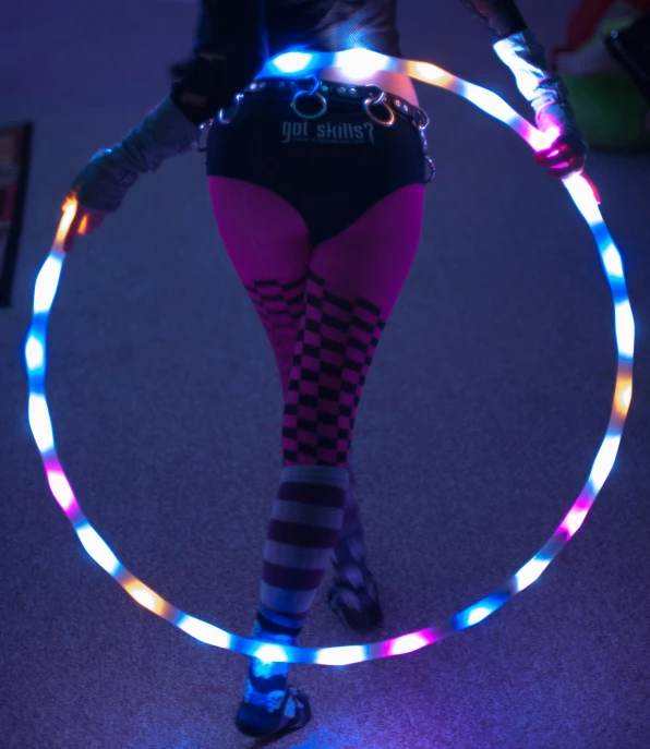 a woman in tights holding a colorful light up hula hoop