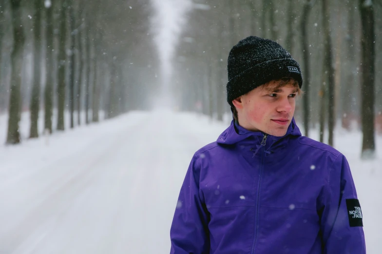a boy standing in front of trees and a frozen road
