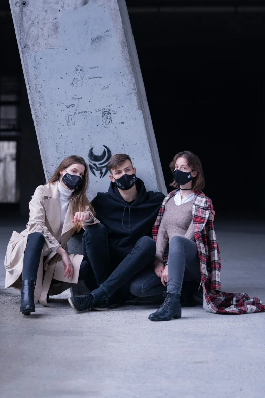 three people sitting down in front of a skateboard with masks on