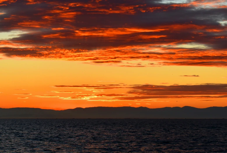 the sun set over the mountains in the water