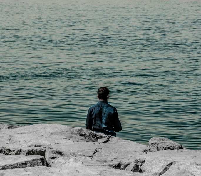 a person sits on rocks by the water