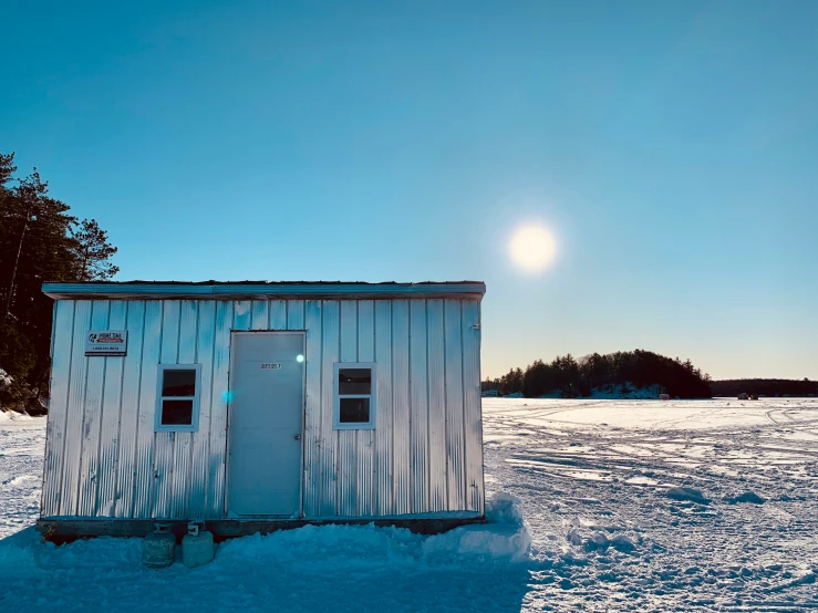 a small metal shed sitting in the middle of a snow covered field