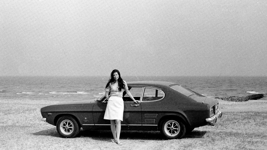 a woman posing beside a parked car on the beach