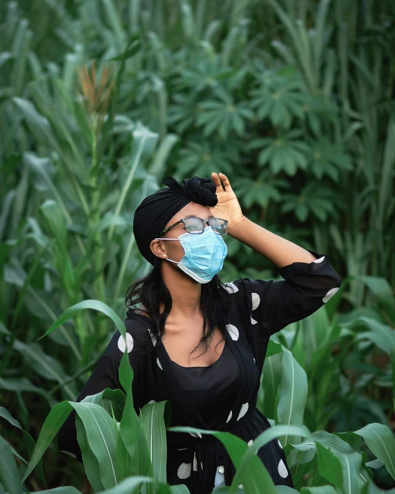 a woman in black and white standing on a corn field wearing a face mask