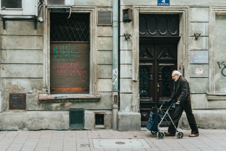 an elderly man walking with a walker down a city sidewalk