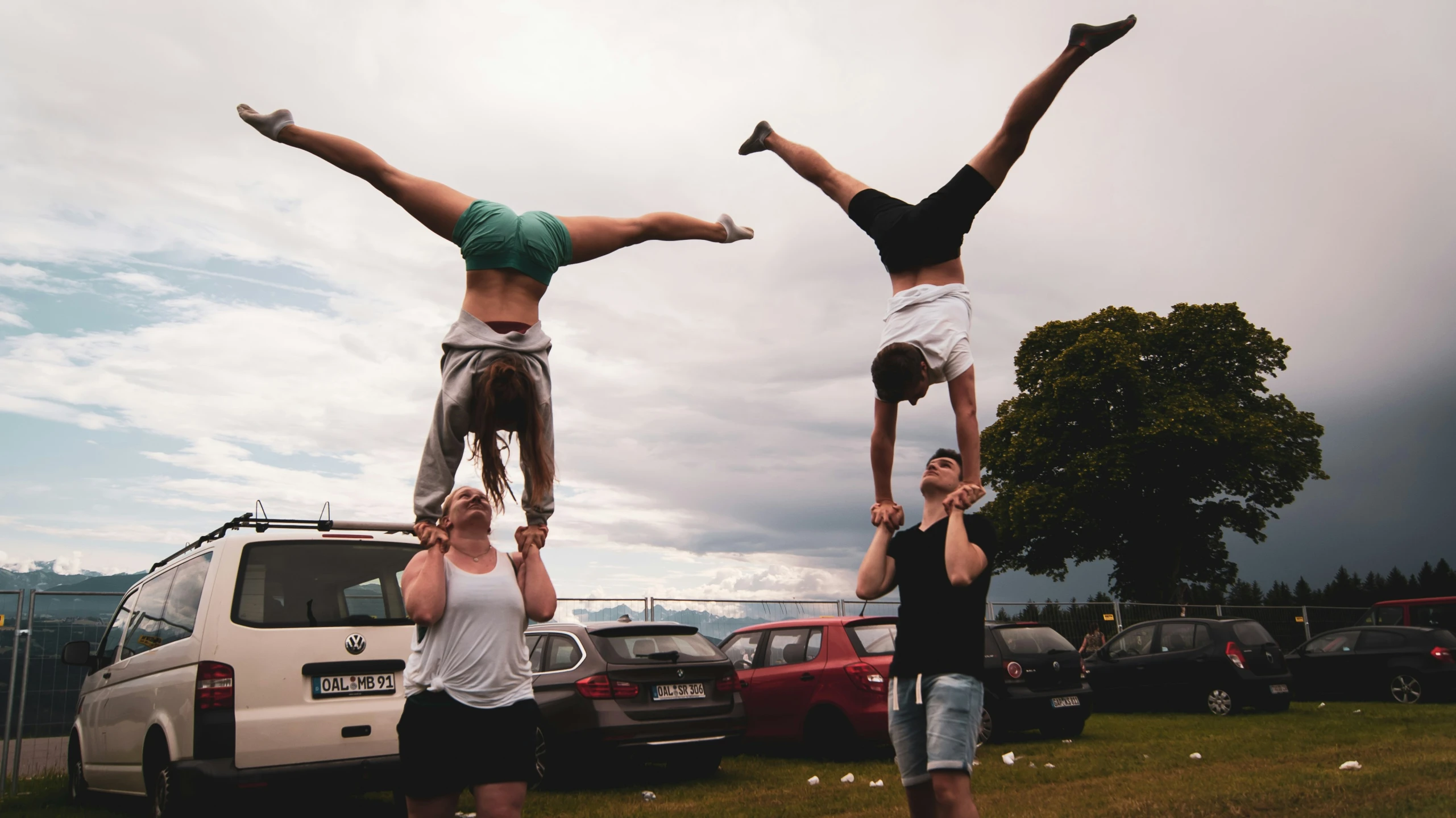 three people doing handstands in front of parked cars