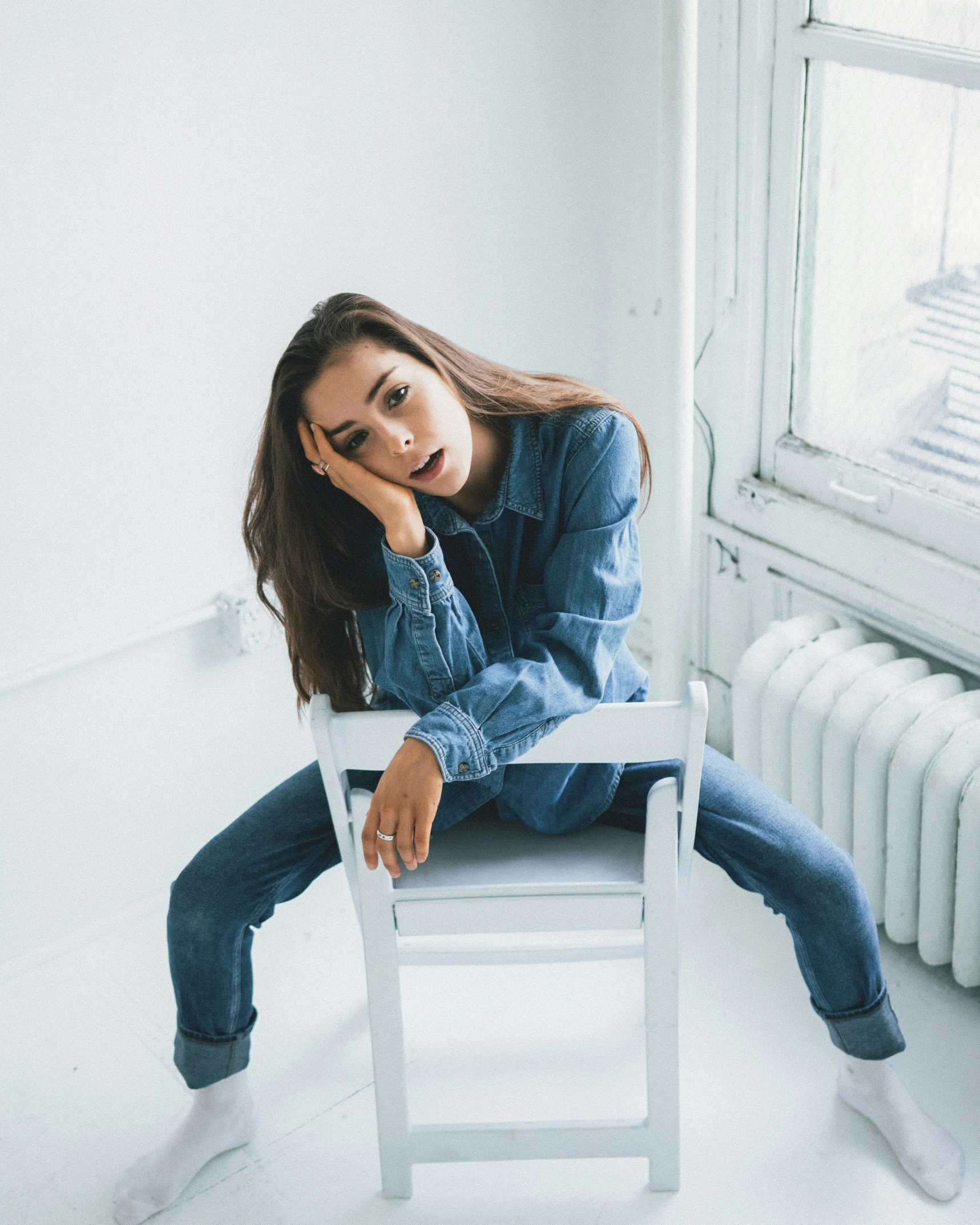 a woman sits on a white chair in a room with white walls