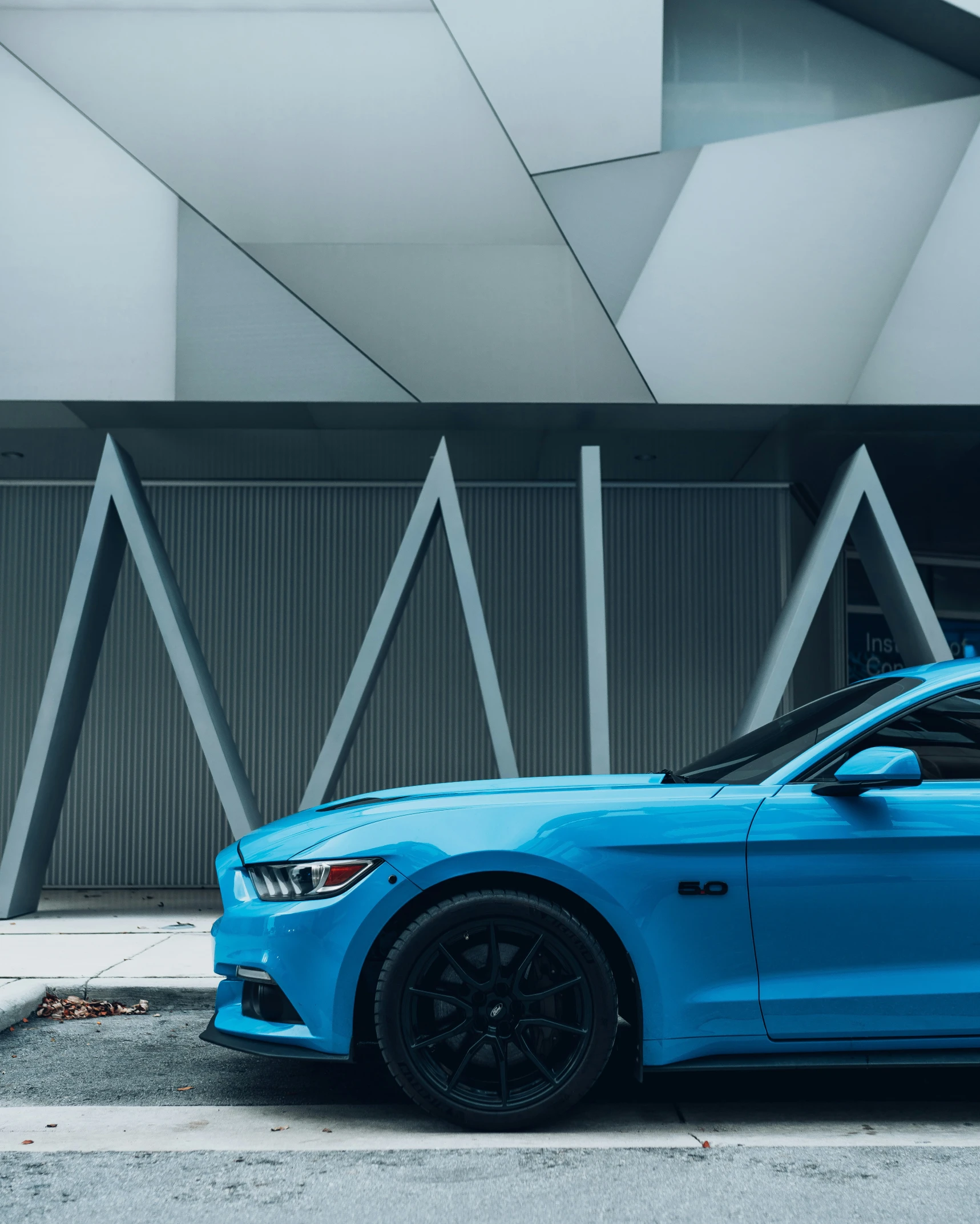 a light blue mustang parked in front of a tall building