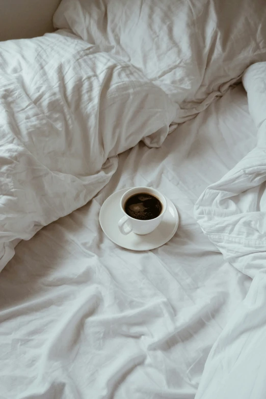 a cup of coffee sits on a messy bed