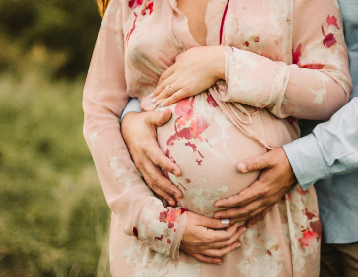 a couple is holding their pregnant daughter while standing near the grass