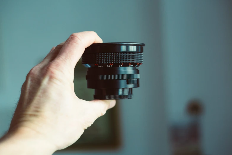 a person holding up a camera lens, with focus on it