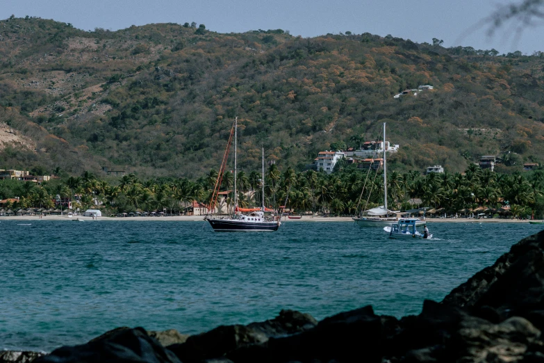 boats docked at the beach in front of a forested mountain