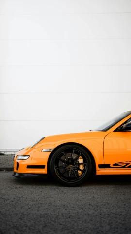 an orange sports car in front of a large wall