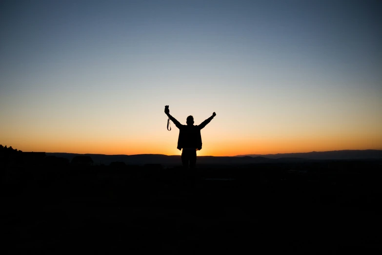 man at dusk with arms raised above head