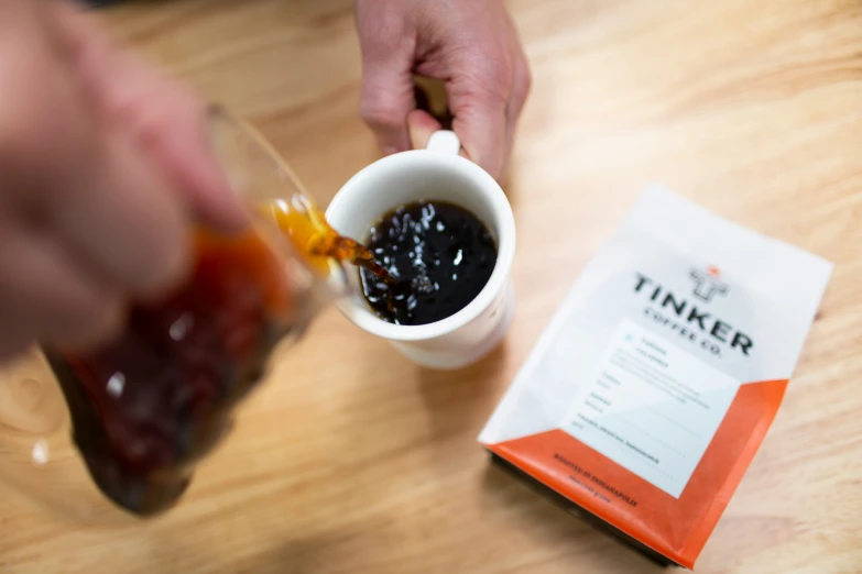 a man putting syrup on a cup sitting next to a packet of tea