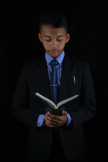 a man in a black suit and tie reading a book