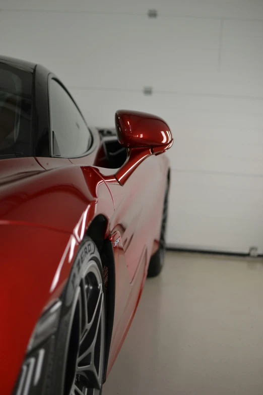 the shiny red car is parked in front of the garage door