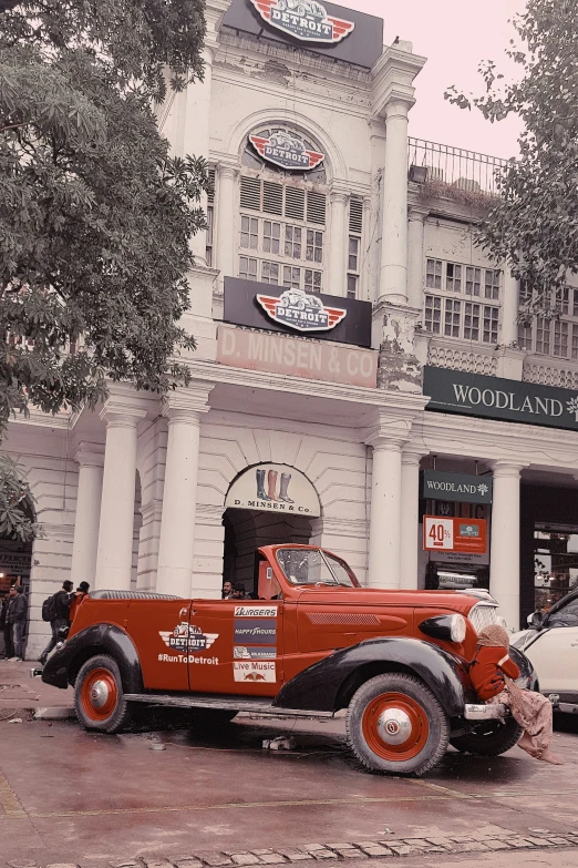 an old red car in front of a very big building