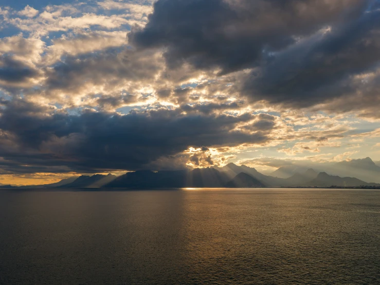 the sun sets over the mountains as clouds cover a body of water