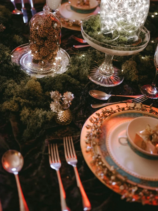 the table is set with glasses, plates and a glass vase